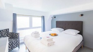 A hotel room with a large bed, a chair, a window, and a breakfast tray on the bed.