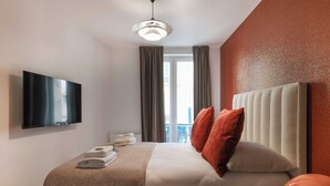 A hotel room with a large bed, a flat-screen TV mounted on the wall, a window with curtains, and a balcony view. - Magnificent apartment - 4BR/10P - Arc de Triomphe (Paris)