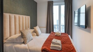A hotel room with a large bed, a flat-screen TV mounted on the wall, and a window with curtains. - Magnificent apartment - 4BR/10P - Arc de Triomphe (Paris)