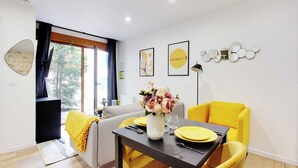 A modern dining area with a table set for two, a yellow armchair, and a sofa in the background.