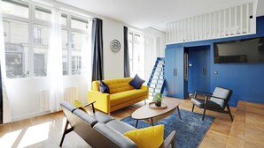 Uma sala de estar moderna com um sofá amarelo, um sofá de couro preto e uma parede azul de destaque.