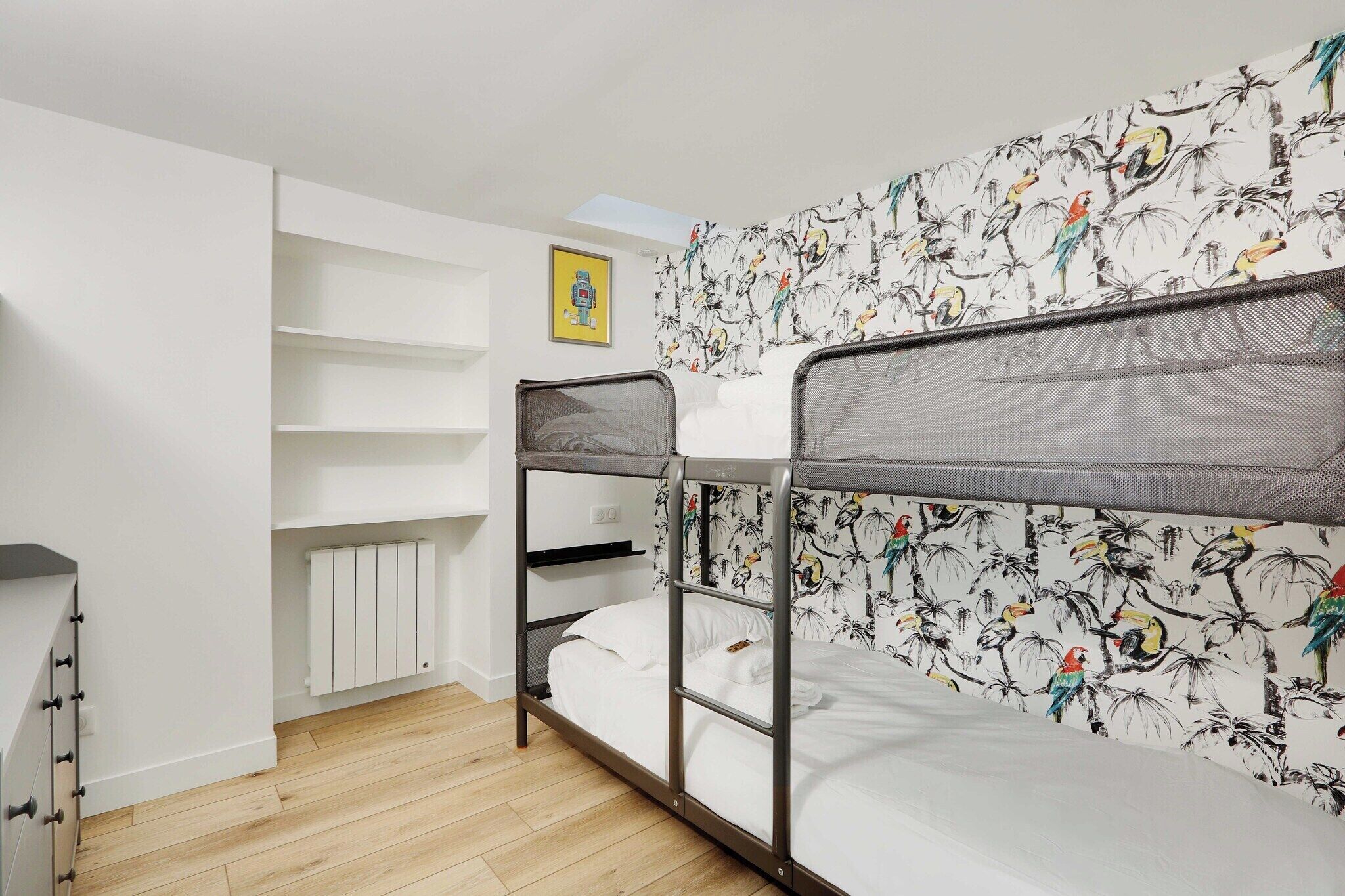 A bunk bed with a tropical bird wallpaper, a white radiator, and a shelf unit.