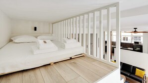 Quarto moderno com cama, cortinas brancas e vista para a cozinha.