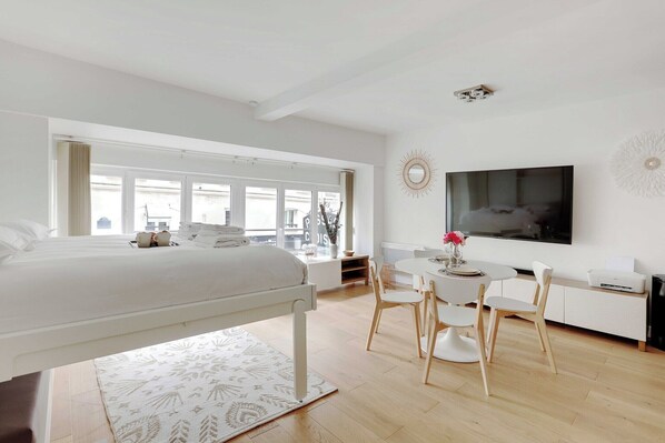 Een moderne hotelkamer met een groot bed, een zithoek met een tafel en stoelen, een aan de muur bevestigde televisie en grote ramen voor natuurlijk licht.
