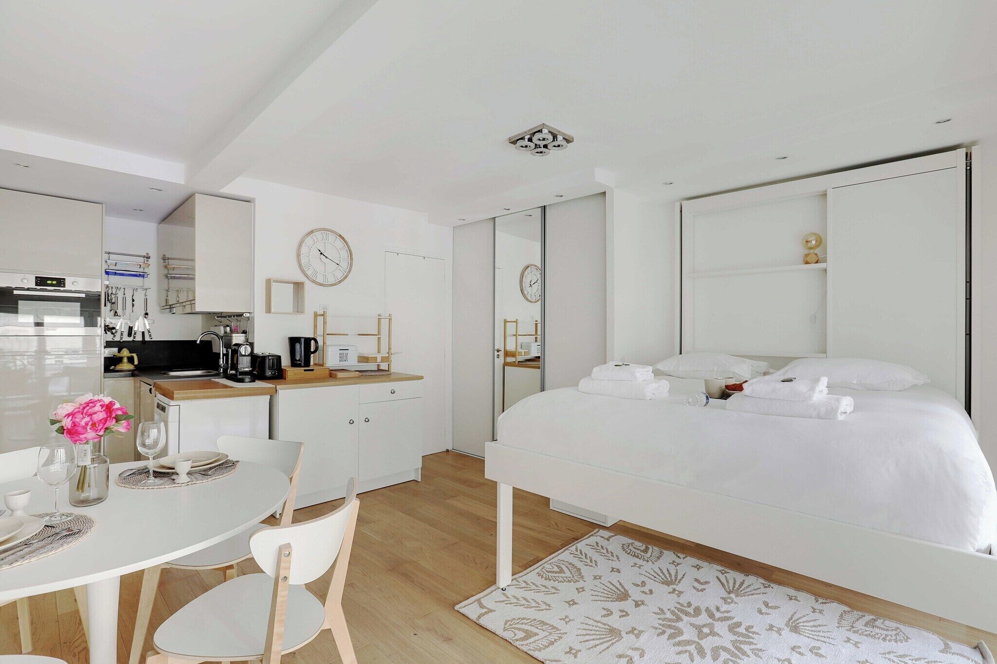 A modern hotel room with a bed, a small kitchen area, and a dining table.