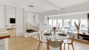 Moderni hotellihuone, jossa on sänky, ruokailutila ja suuri ikkuna, josta avautuu näkymä kaupunkiin.