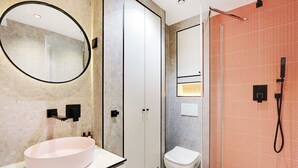Ein modernes Badezimmer mit rundem Spiegel, Waschbecken in Weiß, Toilette und Duschbereich.