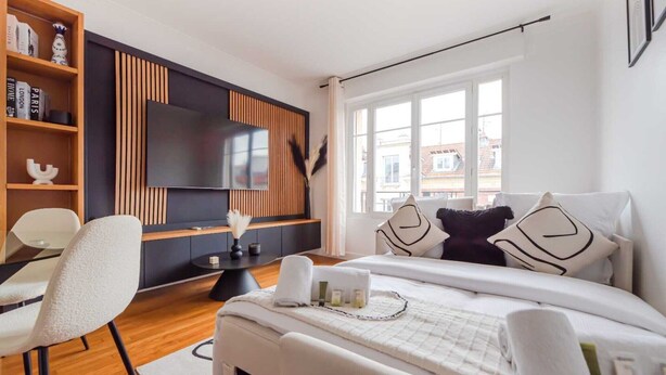 A modern hotel room with a bed, a desk, a chair, a TV, and a bookshelf.