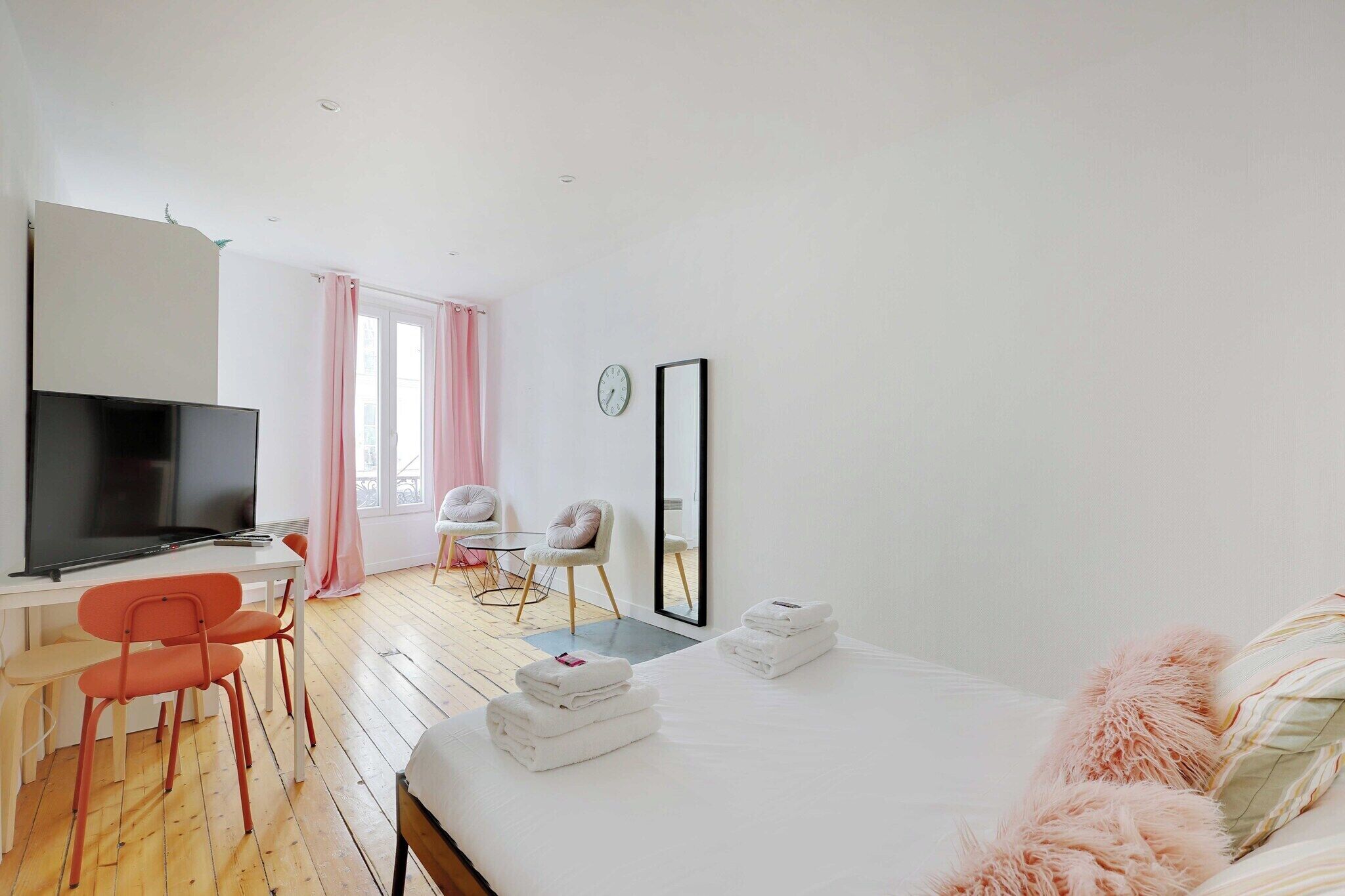 Une chambre d’hôtel moderne, équipée d’un lit, d’un bureau avec une télévision, d’une chaise, d’une petite table et d’une fenêtre avec des rideaux.