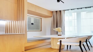 Un comedor moderno con un banco de madera, una mesa redonda y un jarrón con flores secas.