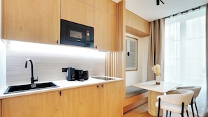 Una cocina compacta con armarios de madera, microondas integrado, un lavamanos y un pequeño comedor con dos sillas.