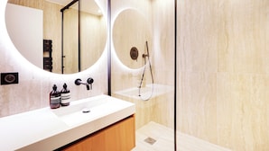 Un baño moderno con un espejo grande, una ducha y un lavabo con dos botellas de champú.