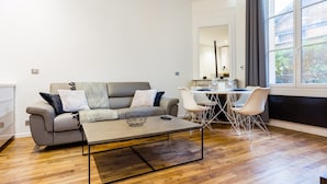 A modern living room with a grey sofa, a coffee table, and a dining area with a white table and chairs.