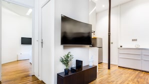 A modern living room with a large flat-screen TV mounted on the wall, a dark wooden console table with a potted plant, and a white cabinet with drawers.