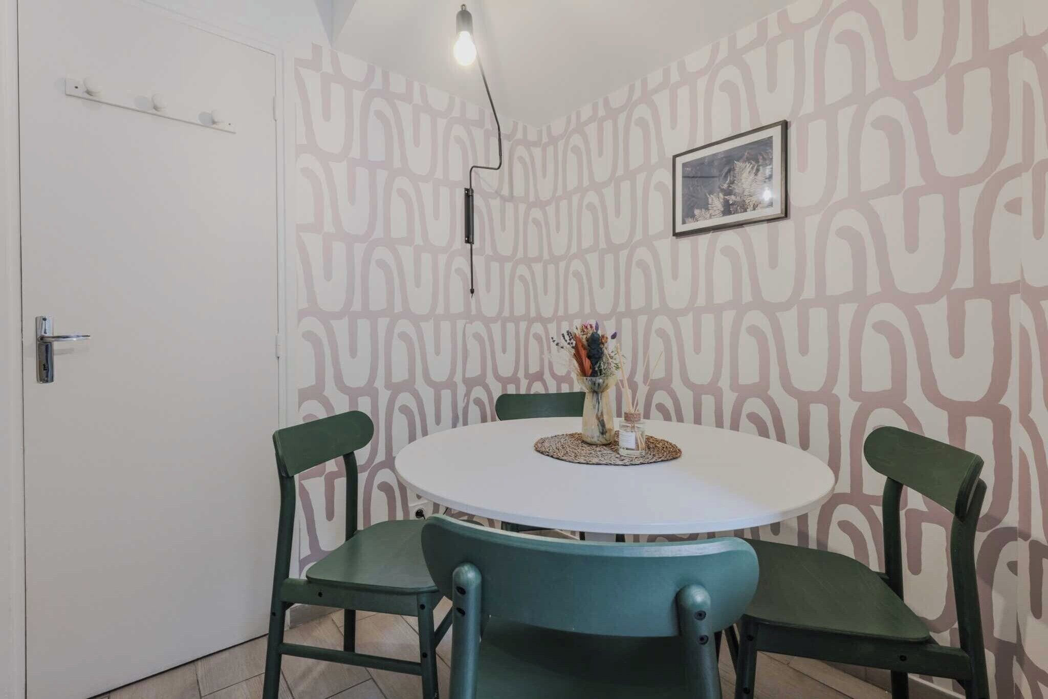 A dining area with a round table, four chairs, a vase with flowers, and a wall with a geometric pattern.