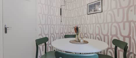 A dining area with a round table, four chairs, a vase with flowers, and a wall with a geometric pattern.