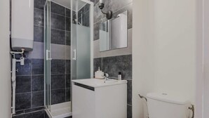 Un baño moderno con cabina de ducha de vidrio, lavamanos blanco y un inodoro.