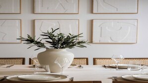 Una mesa de comedor dispuesta con platos, vasos y cubiertos, rodeada de sillas de mimbre.