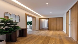 Un pasillo con suelo de madera, una planta en maceta y un banco. Hay puertas de madera y un espejo en la pared.