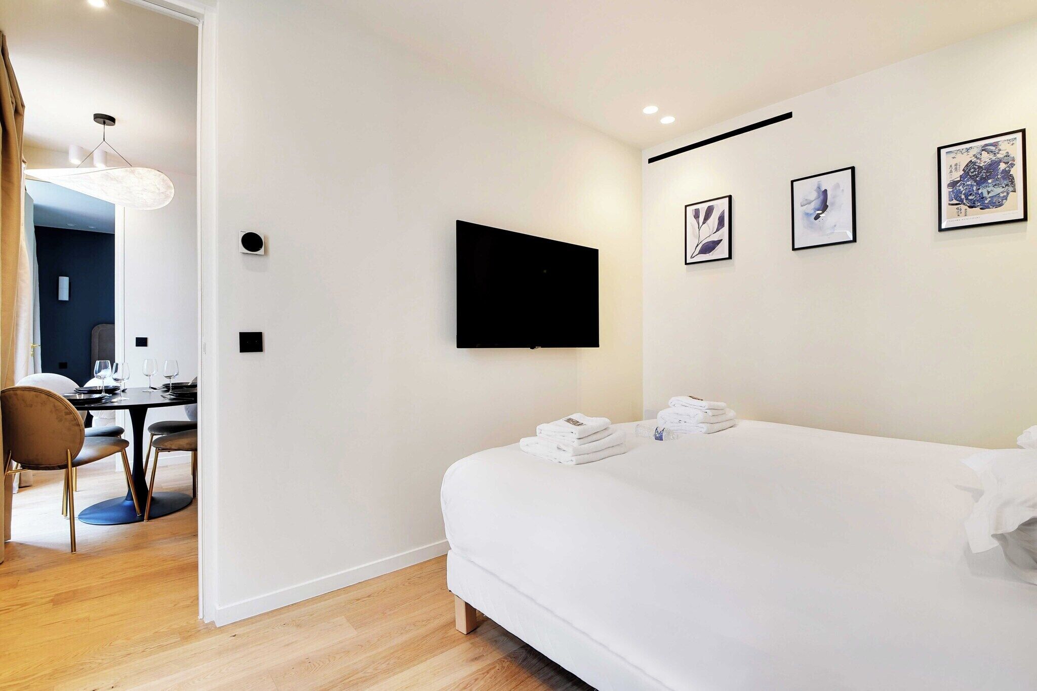 Una habitación de hotel moderna con una cama grande, un televisor de pantalla plana en la pared y una zona de comedor con mesa y sillas.