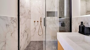 A modern bathroom with marble walls, a glass-enclosed shower, and a minimalist sink area.