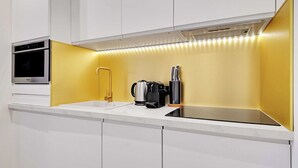 A modern kitchen with white cabinetry, a built-in oven, a coffee maker, and a kettle on the counter.