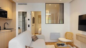 A modern living room with a sofa, a dining table, a TV, and a kitchen area with a microwave and sink. - Beautiful Apartment - 1BD/4P - Quartier Latin (Paris)