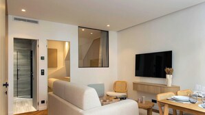 A modern hotel room with a sofa, a dining table set with plates and glasses, a flat-screen TV mounted on the wall, and a staircase leading to another level. - Beautiful Apartment - 1BD/4P - Quartier Latin (Paris)