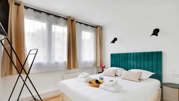 Een hotelkamer met een bed, een raam met gordijnen, een nachtkastje en een wandlamp.