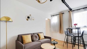 Een moderne woonkamer met een bank, een klein rond tafeltje, een vloerlamp en een eethoek met stoelen en een tafel.