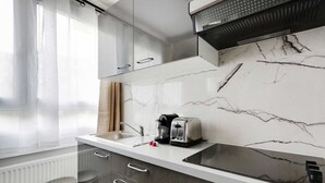 Een moderne keuken met een marmeren spatwand, roestvrijstalen apparatuur en een raam met transparante gordijnen.