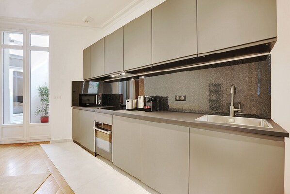 A modern kitchen with a built-in oven, microwave, and stainless steel sink. - Superb apartment with terrace 2BR/4P Trocadero (Paris)