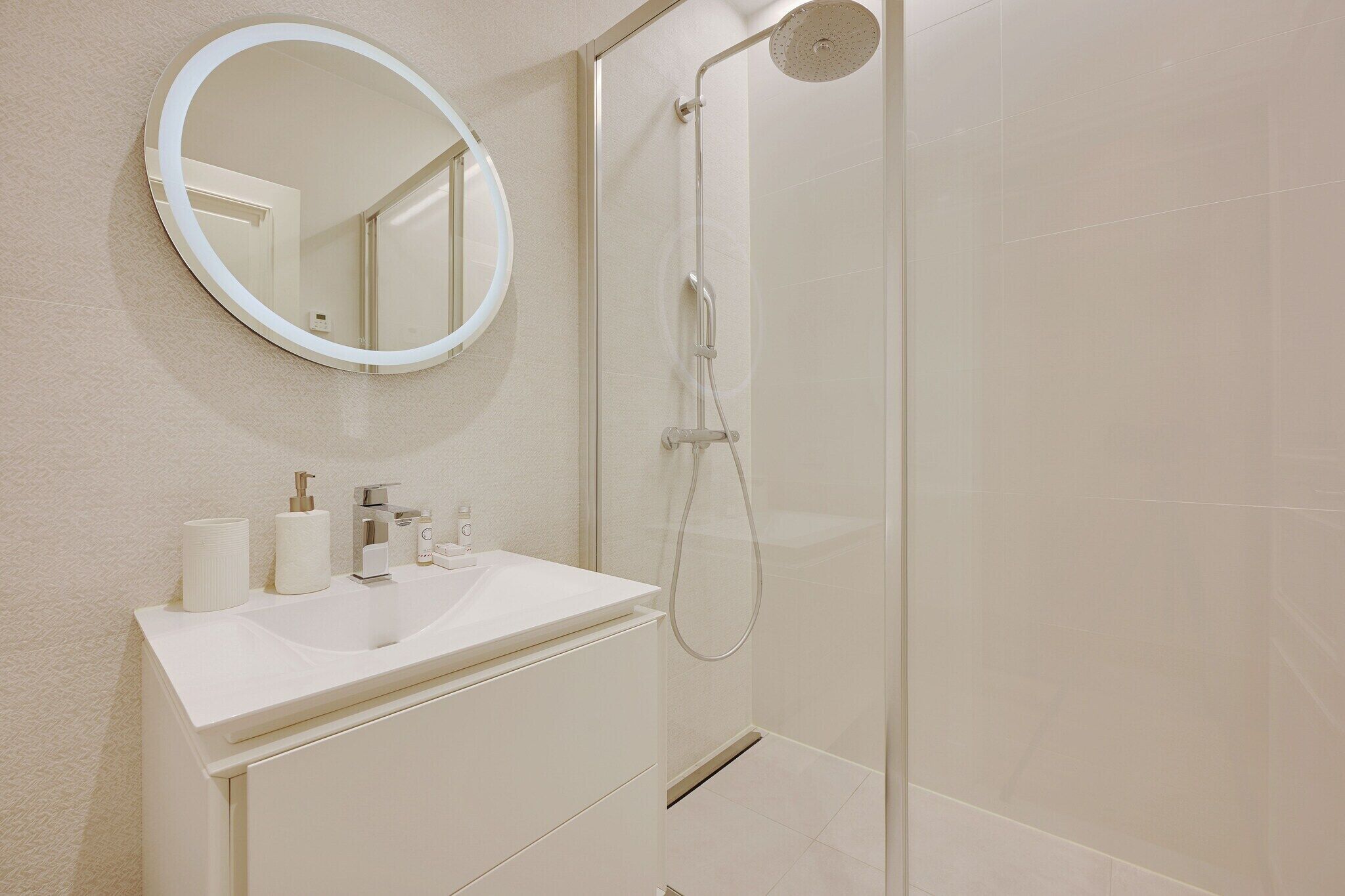 A bathroom with a white sink, a round mirror, and a glass-enclosed shower.