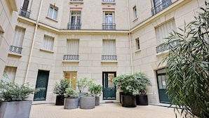 A courtyard with a tiled floor, potted plants, and a building facade with windows and balconies. - Superb apartment with terrace 2BR/4P Trocadero (Paris)