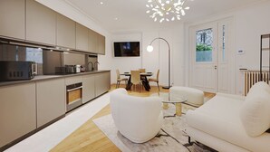 A modern kitchen with built-in appliances, a dining area with a glass table, and a living room with a white sofa and a unique light fixture. - Superb apartment with terrace 2BR/4P Trocadero (Paris)