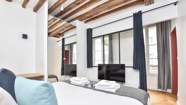 Camera d'albergo moderna con soffitto in legno, un letto grande con asciugamani ordinatamente piegati, una TV a schermo piatto e una finestra con tende.