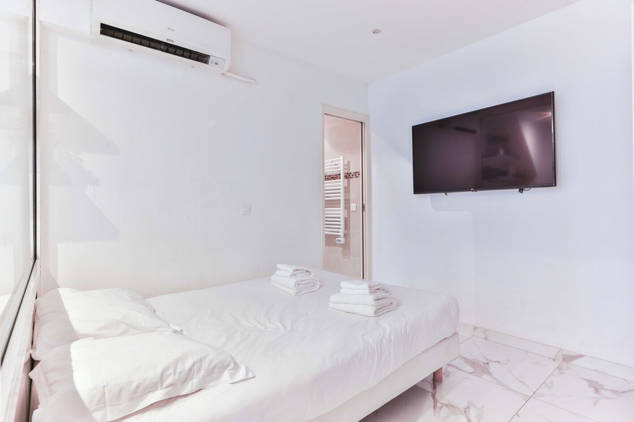 Quarto de hotel com uma cama, uma TV de tela plana na parede e um aparelho de ar condicionado sobre a cama.