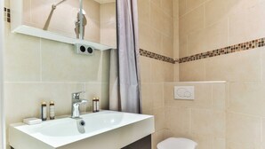 Ein Badezimmer mit einem weißen Waschbecken, einem Spiegel, einer Dusche und einer Toilette.