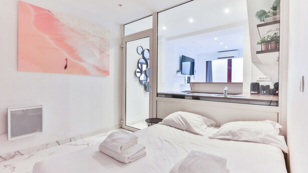 Ein modernes Hotelzimmer mit einem großen Bett, einem durch eine Glastür einsehbaren Badezimmer und einem großen Spiegel, der den Raum reflektiert.