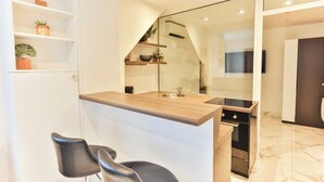 Eine moderne Küche mit einer Holz Arbeitsplatte, einem eingebauten Backofen und einer Glastrennwand. Zwei schwarze Stühle und ein kleines Regal mit Pflanzen sind ebenfalls vorhanden.