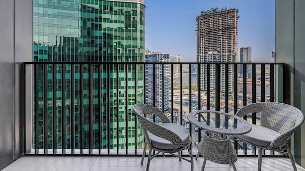 Een balkon met twee rieten stoelen en een klein tafeltje, met uitzicht op een stadsbeeld met moderne gebouwen.