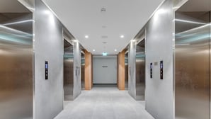 Een modern liftinterieur met metalen wanden, een betegelde vloer en bedieningspanelen aan de wanden.