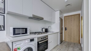 Een kleine keuken met witte kasten, een magnetron, een fornuis, een wasmachine en een houten deur.
