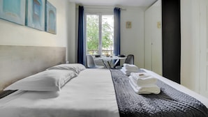 A hotel room with a bed, a desk, and a chair. There is a window with curtains, a door, and artwork on the wall. - Peaceful Studio -2P- Gare de l'Est/République (Paris)