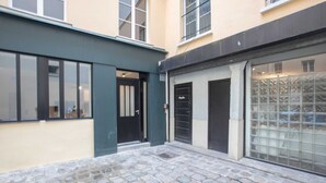Un patio con suelo adoquinado, una puerta negra y una puerta de vidrio con diseño de cuadrícula.