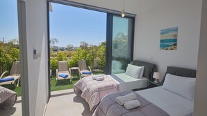 A bedroom with two beds, a balcony with chairs, and a painting on the wall. - Protaras Aqua Pearl Villa Aq11 (Paralimni)