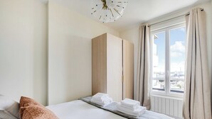 Een hotelkamer met een bed, een houten garderobe, een raam met gordijnen en uitzicht op de stad.