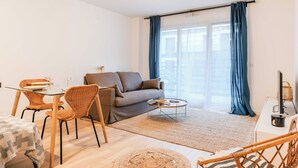 A modern living room with a sofa, two wicker chairs, a glass dining table, and a coffee table. - Classy appartement - Flea Market (Saint-Ouen-sur-Seine)