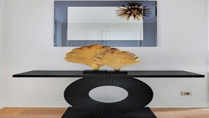 Un interior modern amb una taula consola negra, un mirall gran i una peça decorativa en forma de sol sobre aquesta.
