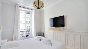 Een hotelkamer met een bed, een aan de muur bevestigde televisie, een stoel en een raam met gordijnen.